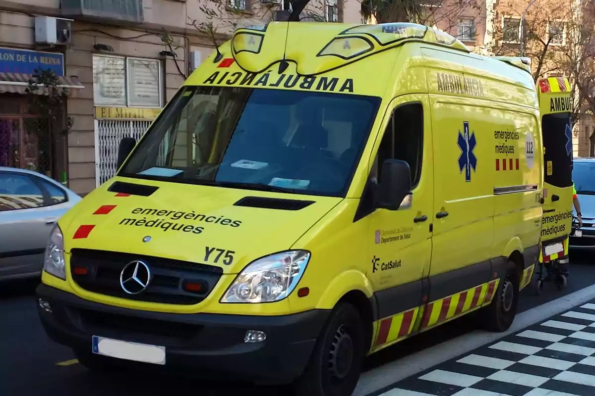 Una ambulancia amarilla con la inscripción "emergències mèdiques" en catalán está estacionada en una calle urbana.