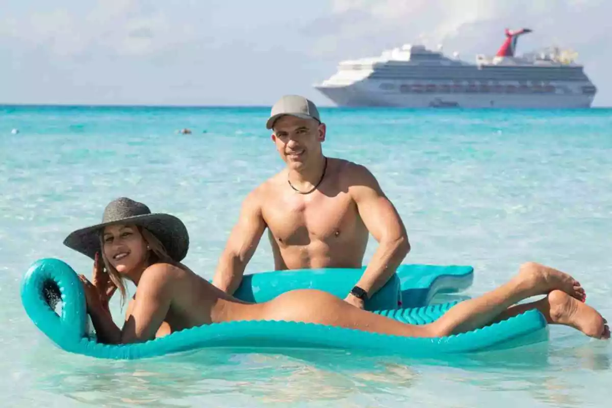 Imágen de una pareja nudista en la playa con el crucero nudista de fondo