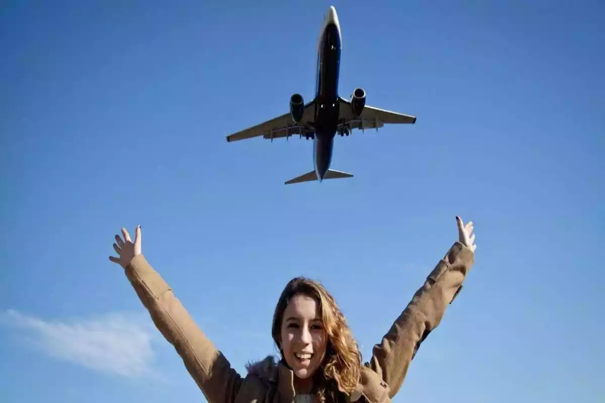 Una chica levanta los brazos y sonríe mientras pasa un avión por encima