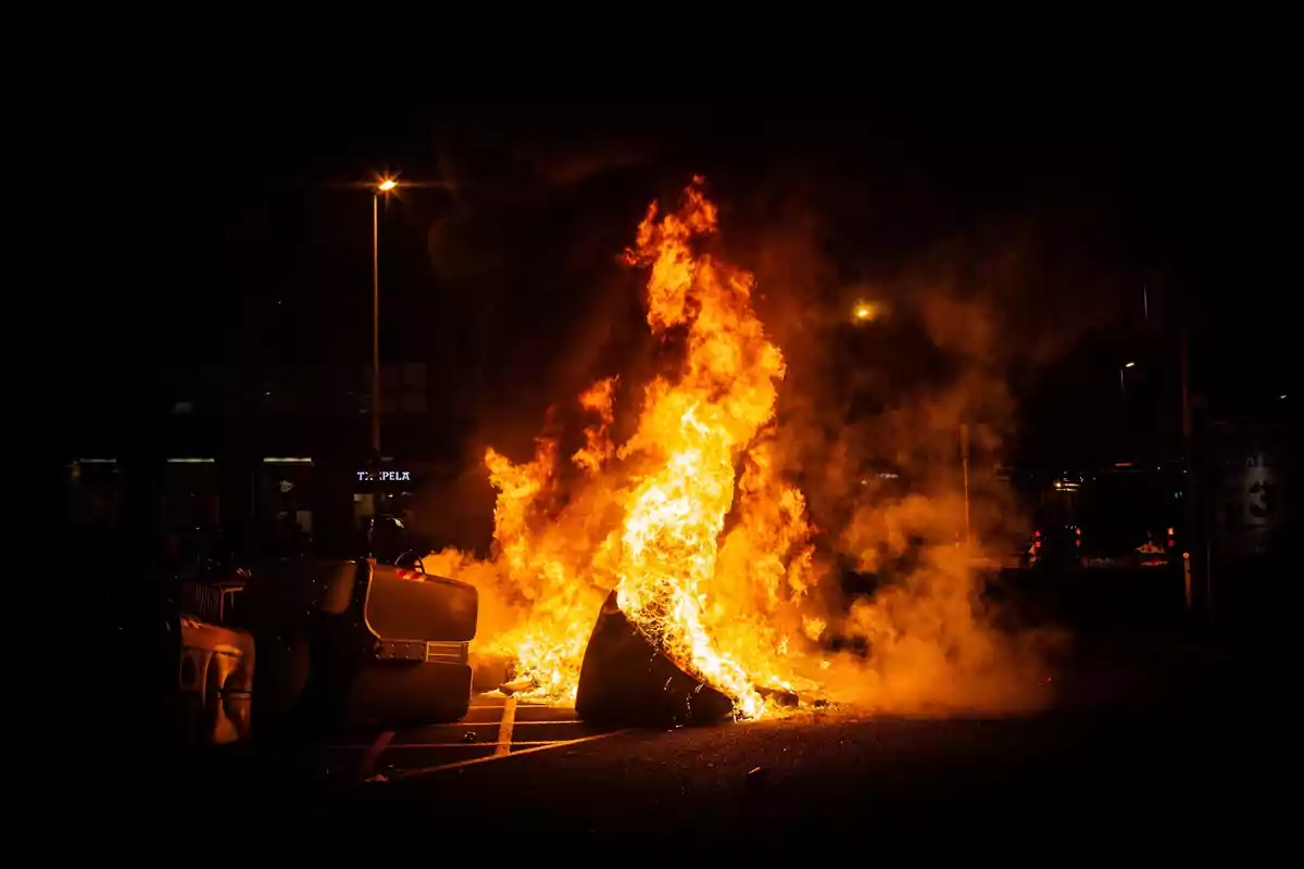 Un coche en llamas en una calle durante la noche.