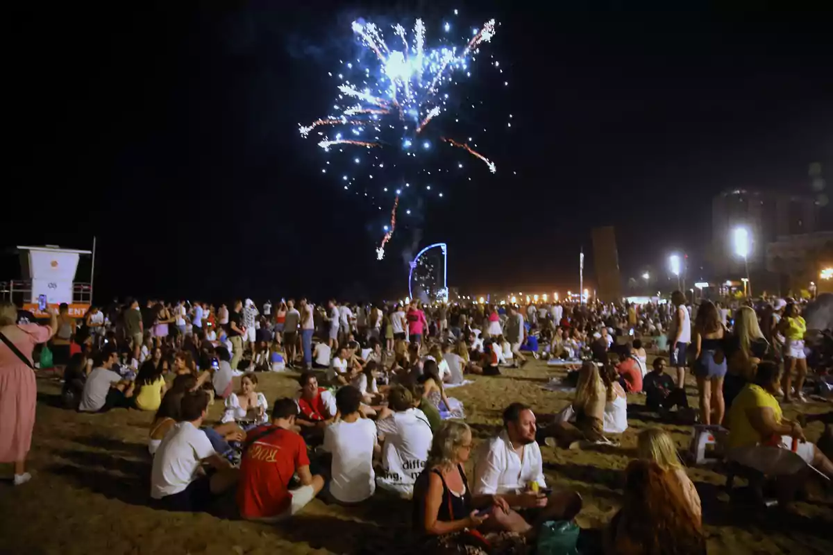 Una multitud disfruta de fuegos artificiales en la playa durante la noche.