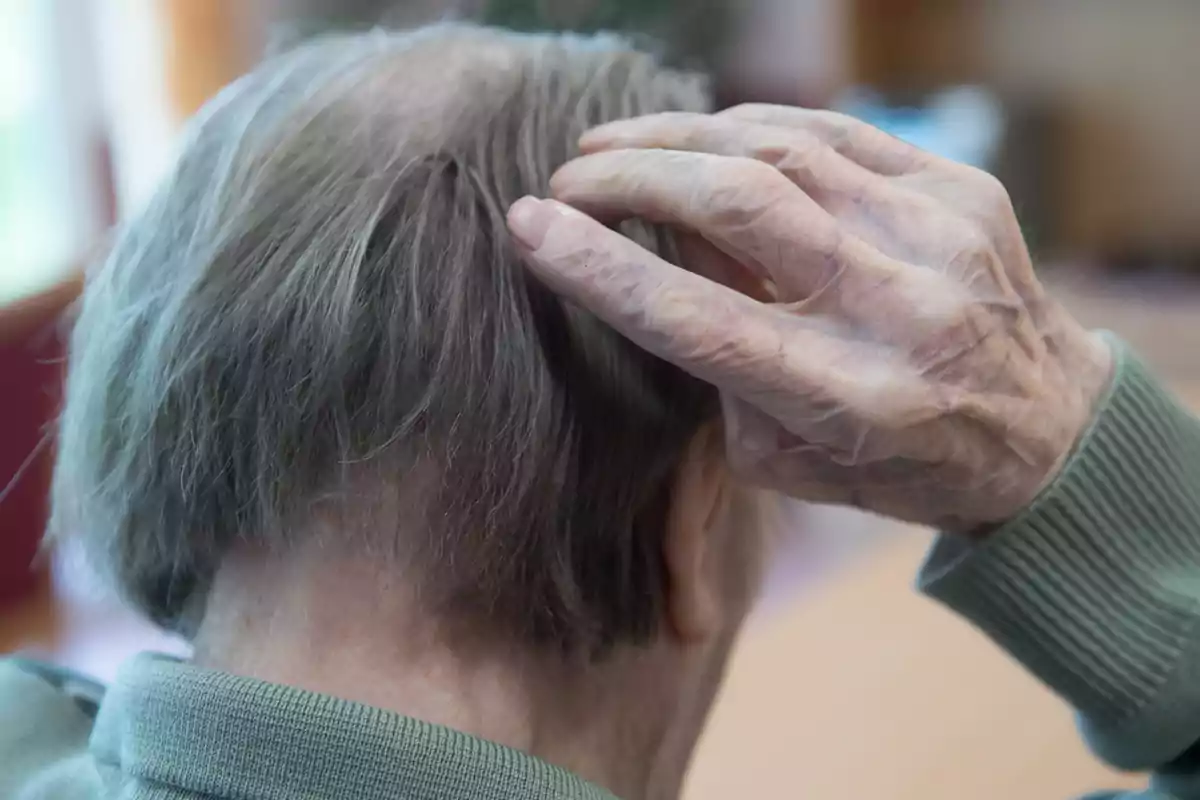 Una persona mayor se rasca la cabeza mostrando signos de envejecimiento en la piel de su mano.