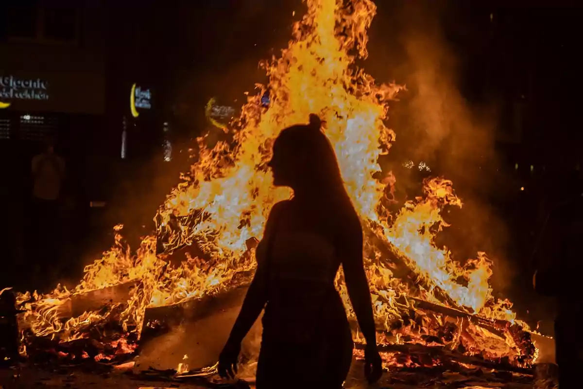 Una mujer pasa delante de la hoguera del barrio de Sant Antoni durante la noche de San Juan, a 23 de junio de 2023