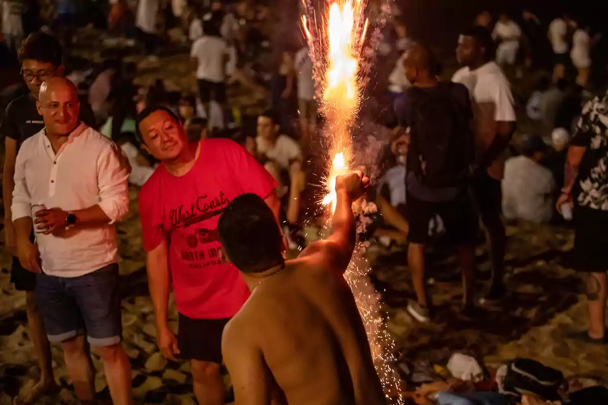 Personas disfrutando de una fiesta nocturna en la playa con fuegos artificiales.