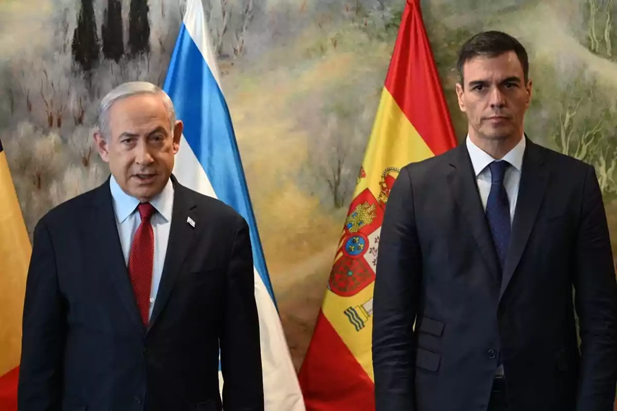 Dos hombres de traje posan frente a las banderas de Israel y España.