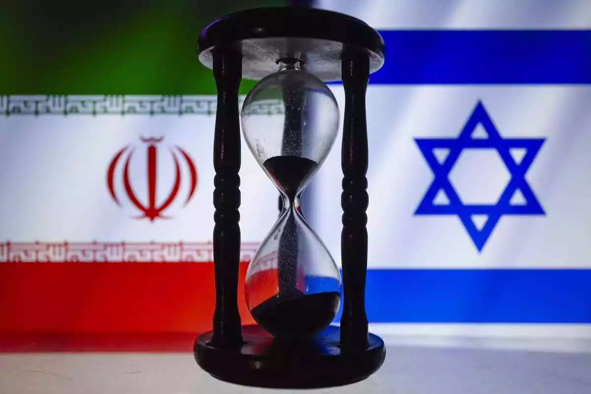 Banderas recortadas de Irán e Israel se exhiben detrás de un reloj de arena de madera
