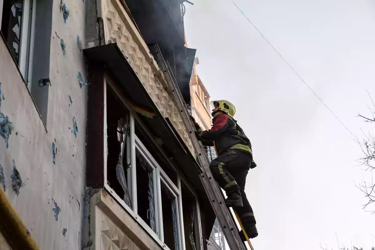 Un bombero sube por una escalera llevando una manguera contra incendios para extinguir el fuego en un edificio después de que Rusia bombardeara Saltivka, un área residencial en Járkov, Ucrania, el 5 de mayo de 2022.
