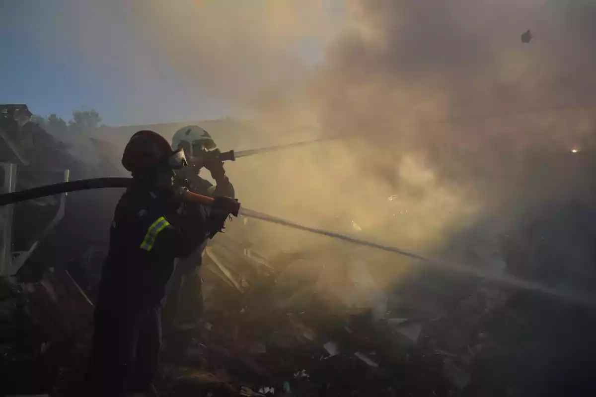 Bomberos combatiendo un incendio en medio de escombros y humo denso.