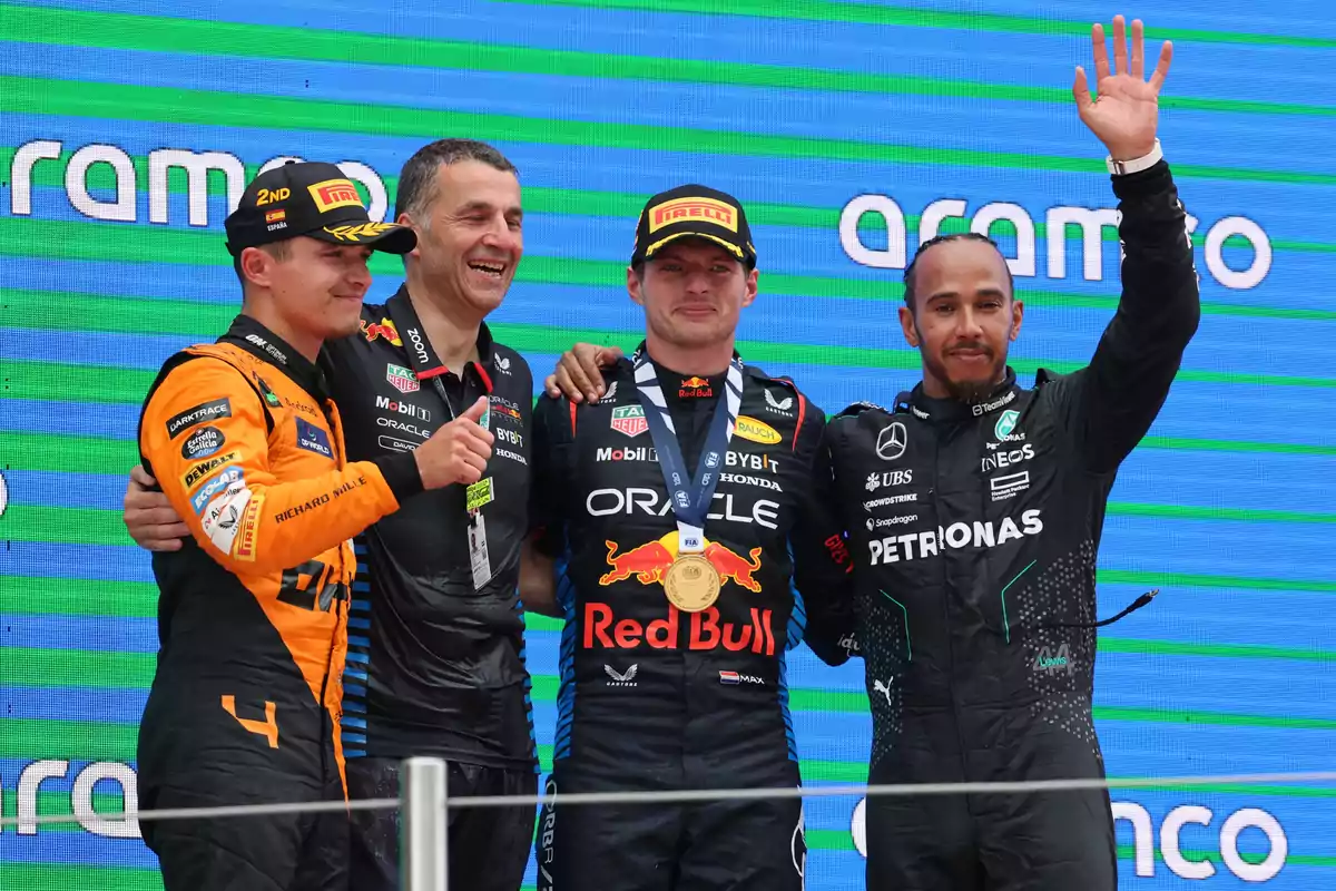 Cuatro personas en un podio de carreras de automovilismo, una de ellas levantando la mano.