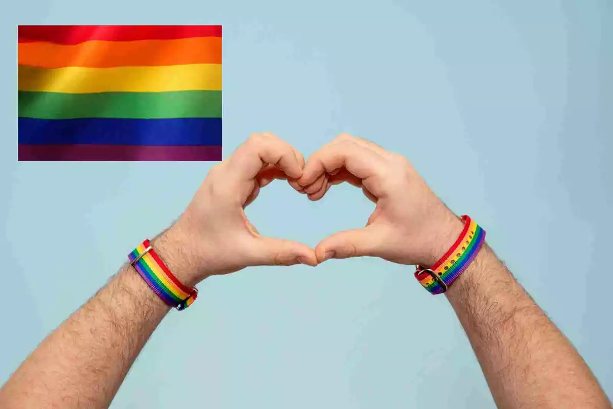 Una bandera LGTB y dos manos formando un corazón